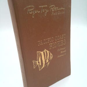 May include: A brown book titled "Pacific Coast Fishes" by Roger Tory Peterson. The cover features a gold illustration of a fish and gold lettering. The book is a field guide.