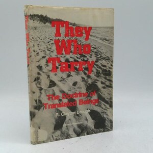 May include: A vintage book titled "They Who Tarry" with red lettering on the cover. The cover features a black and white photograph of a beach scene. The book's subtitle is "The Doctrine of Translated Beings."