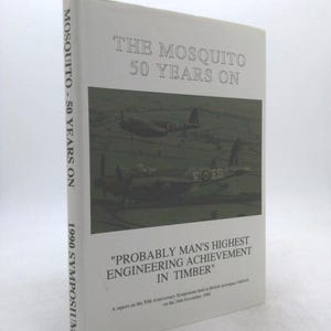 May include: A white book titled "The Mosquito 50 Years On" with an image of two airplanes. The book's spine reads "MOSQUITO - 50 YEARS ON" and "1990 SYMPOSIUM". The cover includes the text "PROBABLY MAN'S HIGHEST ENGINEERING ACHIEVEMENT IN TIMBER".
