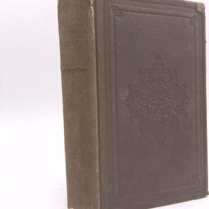 May include: A brown hardback book with a decorative design on the front cover. The book has a spine with raised lettering and a worn appearance.