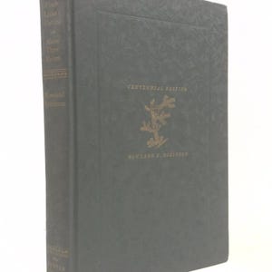 May include: A hardcover book titled "Uncle Lisha's Outing and Along Three Rivers" by Rowland E. Robinson. The cover is dark green with gold lettering and a gold emblem. The spine also features gold lettering.