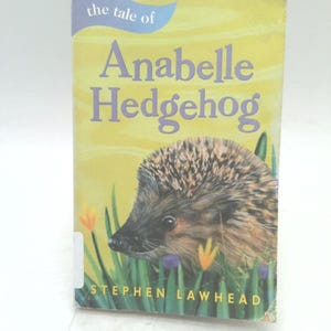 May include: A children's book titled "The Tale of Anabelle Hedgehog" with a yellow cover. The cover features a detailed illustration of a hedgehog, flowers, and the author's name, Stephen Lawhead.