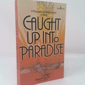 May include: A hardcover book titled "CAUGHT UP INTO PARADISE" with a light orange cover and a stylized illustration. The book's title is in large, bold letters. The author's name, Richard E. Eby, D.O., is also visible.