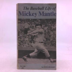 May include: A vintage book titled "The Baseball Life of Mickey Mantle." The cover features a black and white action shot of Mickey Mantle swinging a bat, with a crowd in the background. The book's title is in blue text.