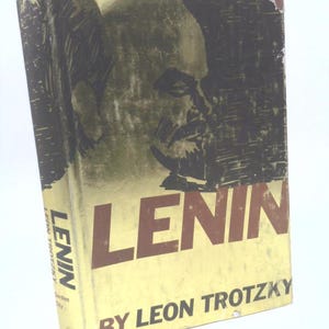May include: A vintage book titled "Lenin" by Leon Trotsky. The cover features a portrait of Lenin in black and olive green against a dark background. The title is in large brown letters on a yellowed background.