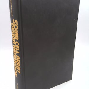 May include: A black hardcover book titled "Solar Cell Array Design Handbook" by  W.  Rauchschbech. The book is on a white background.