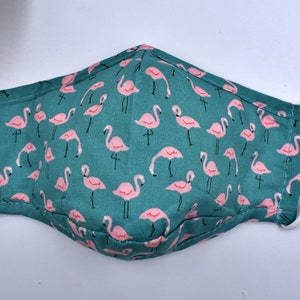 May include: A teal blue face mask with a pink flamingo pattern. The mask has white elastic ear loops.