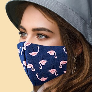 May include: A blue face mask with a pink flamingo pattern. The mask is made of fabric and has a nose wire and ear loops.