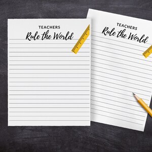 May include: Two white lined sheets of paper with the text "Teachers Rule the World" at the top. A yellow ruler is placed diagonally across the top of each sheet.