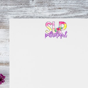 May include: A white card with the text "SLP pathologist" in purple lettering. The letters "SLP" are in a colorful, tie-dye font with a floral design.