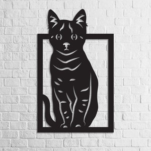 以下が含まれることがあります： 正方形のフレームの中に座っている猫のシルエットが描かれた黒い金属製の壁飾り。猫は正面を向いており、耳はピンと立っていて、尻尾は体の周りに巻かれている。