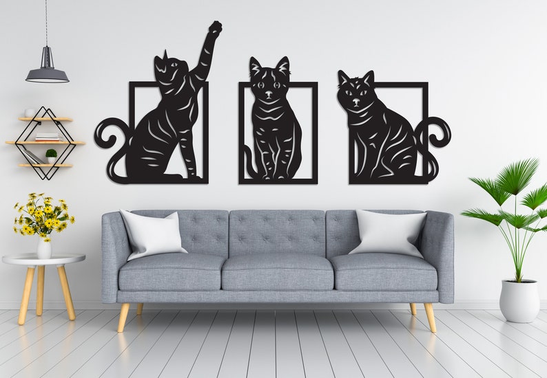 以下が含まれることがあります： 異なるポーズの猫のシルエットが描かれた、黒い金属製の壁飾り3点。各猫は正方形で囲まれています。