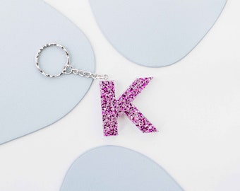 May include: A pink sparkly letter K keyring with a silver chain and ring.