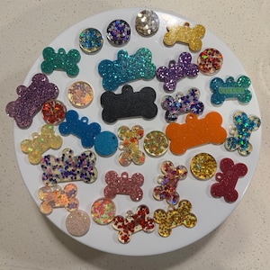 Può includere: Assortimento di ciondoli a forma di osso di cane colorati con glitter incorporati nella resina. I ciondoli sono su una superficie bianca.