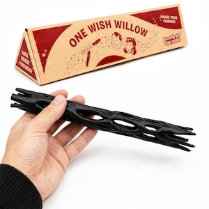 May include: A black, cylindrical, hollow, textured object with an open lattice structure, accompanied by a triangular cardboard box labeled ONE WISH WILLOW, featuring illustrations of two people and the text AMAZE YOUR FRIENDS and YOU ONLY GET ONE WISH.