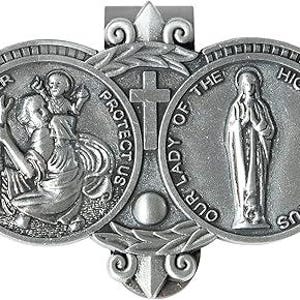 May include: A silver-toned metal visor clip featuring two circular medallions. The left medallion depicts Saint Christopher carrying a child with the text ST. CHRISTOPHER PROTECT US. The right medallion shows a figure with the text OUR LADY OF THE HIGHWAY PRAY FOR US.