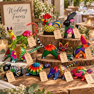 May include: A collection of hand-painted wooden animal figurines including cats, rabbits, armadillos, and turtles, each featuring vibrant floral patterns and a small brown tag printed with "Sofia & Mateo 10.14.2024" next to a wedding sign.