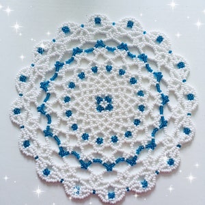 May include: White beaded doily with a blue beaded border. The doily has a circular design with a central motif.