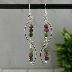 May include: Silver earrings with a curved wire design and green and pink gemstone beads.