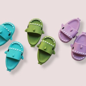 May include: A collection of colorful shark-themed slides in shades of teal, green, and lavender. Each slide features a cartoon shark face with white teeth and black eyes. The slides are arranged on a light pink background.