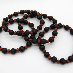 May include: Several black lava stone bead bracelets with alternating reddish-brown wooden beads. The bracelets are arranged in a circular pattern, showcasing the contrast between the dark and light colors. The bracelets are a natural, earthy accessory.
