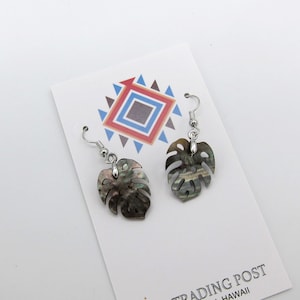 May include: A pair of silver dangle earrings with a black and green iridescent leaf design. The earrings are displayed on a white card with the text "808 TRADING POST HONOLULU, HAWAII".