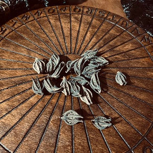 May include: A wooden Ouija board with a black and white alphabet and numbers around the edge. A collection of dried, brown, leaf-like objects are scattered on the board.