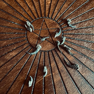 May include: A dark brown, circular, metal decorative piece with a star in the center and radiating lines. Several small, claw-like objects are arranged around the star. The background is a dark wooden surface.