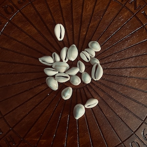 May include: A wooden Ouija board with white shell planchette pieces on a brown wooden surface. The board has letters, numbers, and words printed on it.