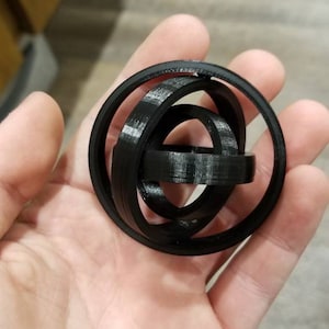 May include: A black 3D printed sphere made of interlocking rings.