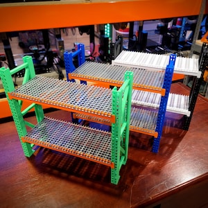 May include: Three colorful metal shelving units with orange, green, and blue frames. Each unit has two shelves with a grid pattern. The shelves are made of a white plastic material.