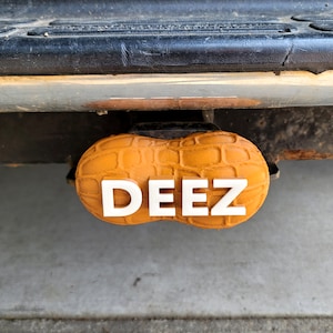 May include: A peanut-shaped hitch cover with the word "DEEZ" printed in white letters.