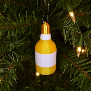 May include: A yellow and white bottle-shaped Christmas ornament hanging on a green artificial Christmas tree.