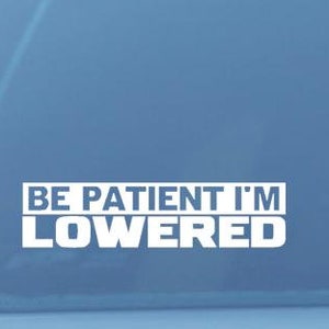 May include: A white vinyl sticker on a car window that reads "BE PATIENT I'M LOWERED".