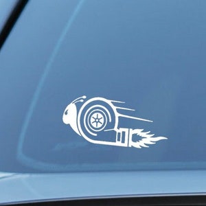 Op de afbeelding: Witte vinyl sticker van een turbolader met vlammen die uit de uitlaat komen. De sticker zit op de achterruit van een auto.