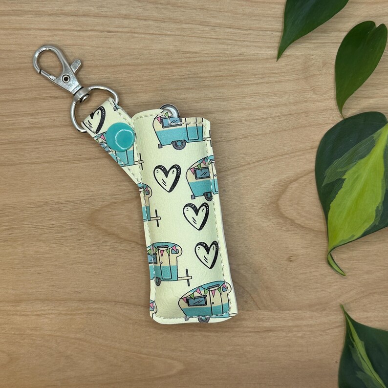 May include: A yellow and blue key chain with a camper van and heart pattern. The key chain has a silver metal clasp.