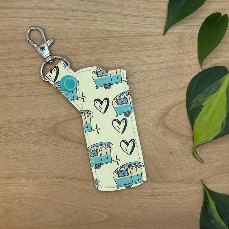May include: A yellow key chain with a blue and white camper van pattern and hearts. The key chain has a silver metal ring and a turquoise button.