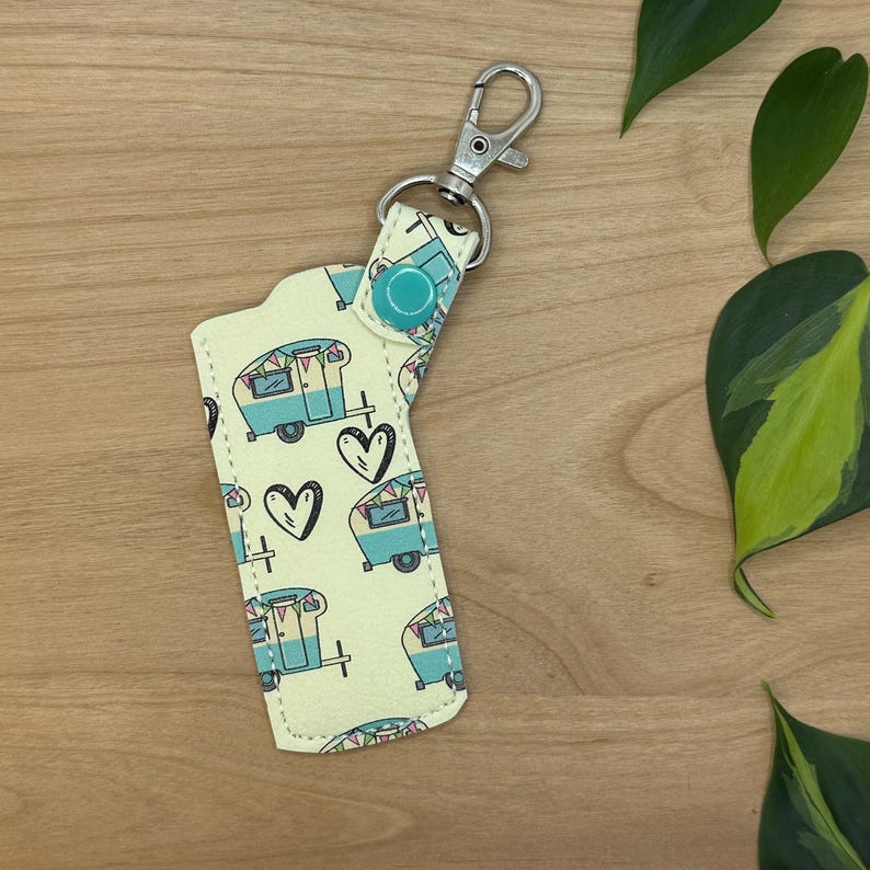 May include: A yellow key chain with a blue and white camper van pattern. The key chain has a silver metal ring and a blue button.