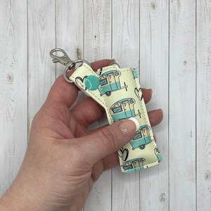 May include: A light blue and white key chain with a camper van pattern. The key chain has a silver metal ring and a turquoise button.