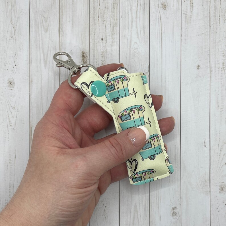 May include: A light blue and white key chain with a camper van pattern. The key chain has a silver metal ring and a turquoise button.
