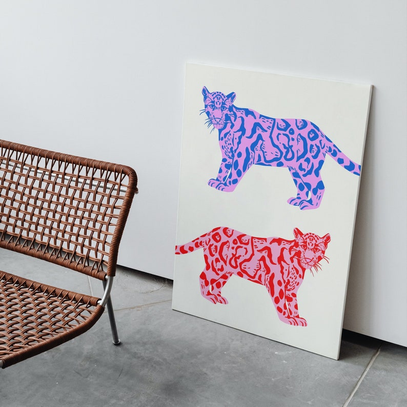 Op de afbeelding: Een witte canvas print met twee gestileerde illustraties van luipaarden. De bovenste luipaard is roze en blauw, en de onderste luipaard is roze en rood.