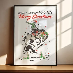 Puede incluir: Impresi&oacute;n enmarcada con tem&aacute;tica navide&ntilde;a. La obra presenta a un vaquero montando un caballo salvaje, con un gorro de Pap&aacute; Noel y una chaqueta verde. El texto dice "Have a Rootin' Tootin' Merry Christmas" en rojo y negro.