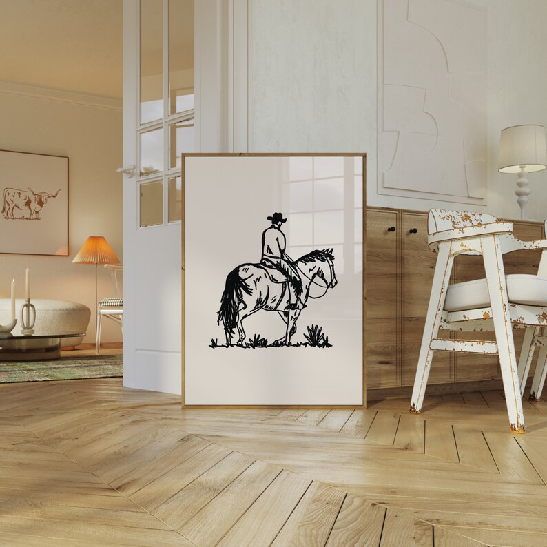Op de afbeelding: Zwart-witte lijntekening van een cowboy die op een paard rijdt. De print is ingelijst en hangt aan een witte muur.
