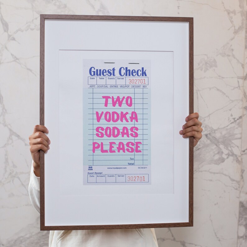 K&ouml;nnte beinhalten: Ein gerahmter Druck eines blauen und wei&szlig;en Gastchecks mit dem Text "TWO VODKA SODAS PLEASE" in Pink. Die Checknummer lautet 302701.