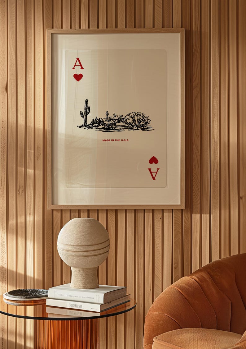 Op de afbeelding: Een ingelijst afdruk van een aas harten speelkaart met een woestijnlandschap en de tekst "Made in the U.S.A.". De afdruk hangt aan een houten paneelwand.