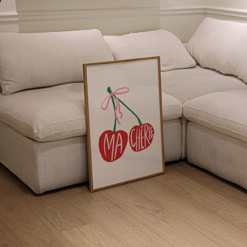 May include: A framed print with a red and green illustration of two cherries with a pink ribbon. The cherries have the words "MA CHERIE" written on them.