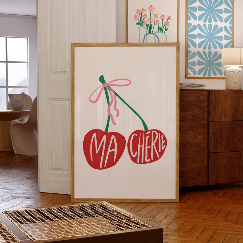 May include: A white poster with a drawing of two red cherries with green stems and a pink ribbon. The cherries have the words "MA CHERIE" written on them.