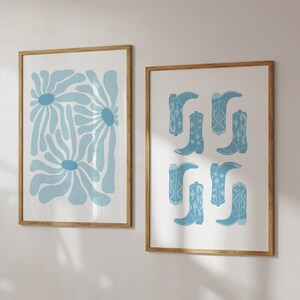 May include: Two framed prints with a light blue color scheme. The print on the left features a stylized abstract design of blue flowers. The print on the right features a pattern of blue cowboy boots with white stars.