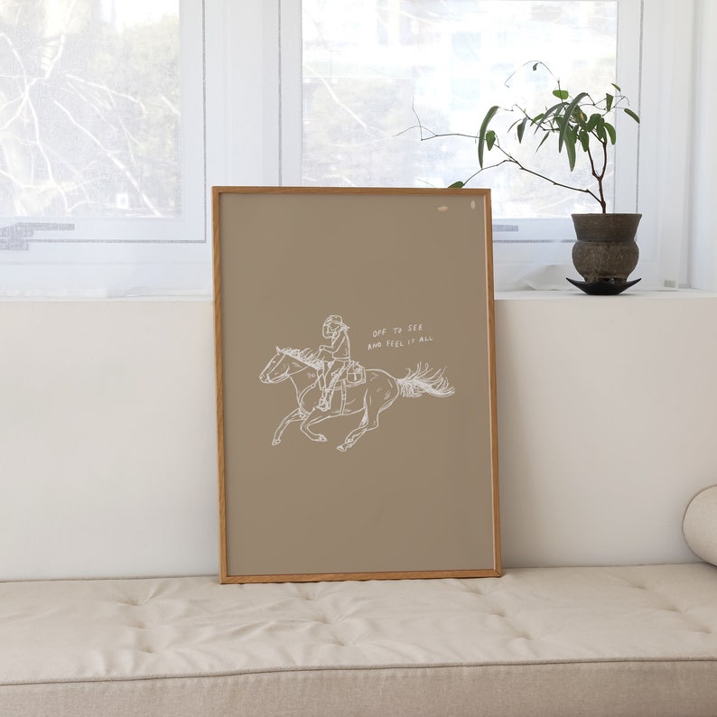 Pu&ograve; includere: Una stampa incorniciata con uno sfondo beige che presenta un disegno a linea di una persona a cavallo. Il testo "Dare to seek and feel it all" &egrave; scritto sotto l'immagine.
