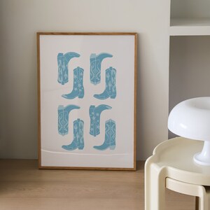 May include: A framed print with a white background and a pattern of blue cowboy boots with white stars and cactus designs.